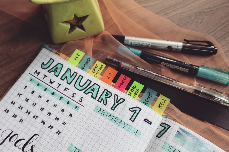 A detailed planner with goals and colorful tabs on a wooden desk with pens.