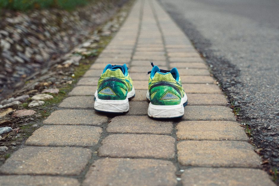 A pair of colorful running sneakers placed on a cobblestone path outdoors, offering a unique perspective.